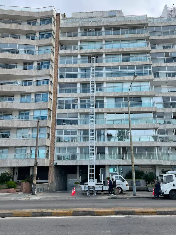 Elevador de altura de Empresa Dante subiendo muebles por el balcón de un edificio frente a la rambla de Montevideo
