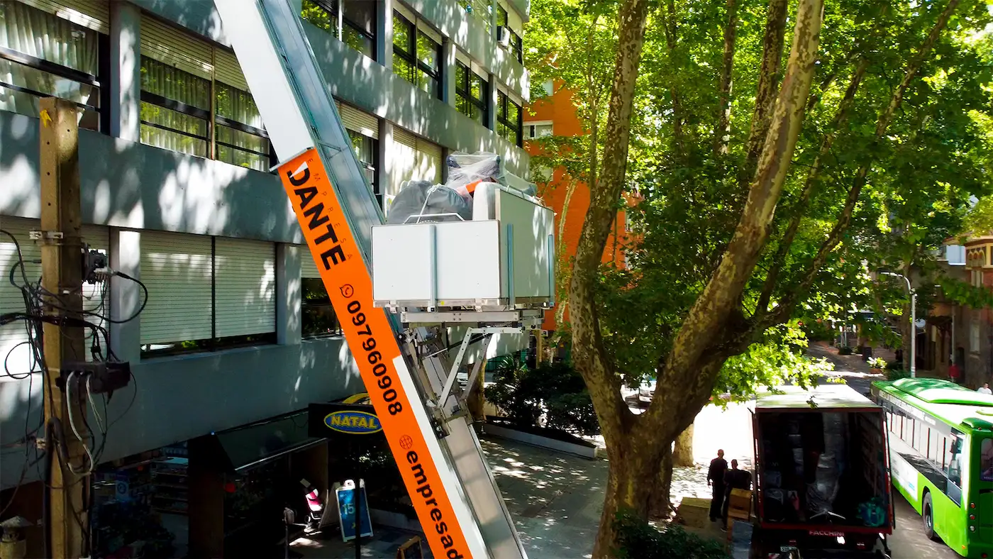 Elevador de altura de Empresa Dante subiendo muebles embalados por la fachada de un edificio en Montevideo