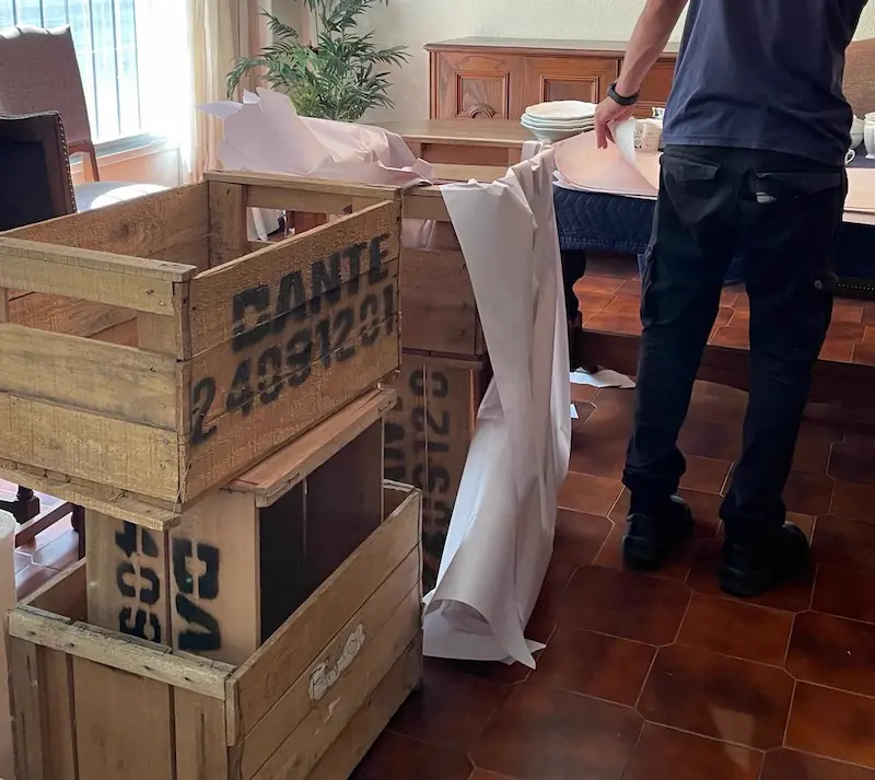 Operario de Empresa Dante envolviendo la vajilla en papel de embalaje junto a los cajones de madera
